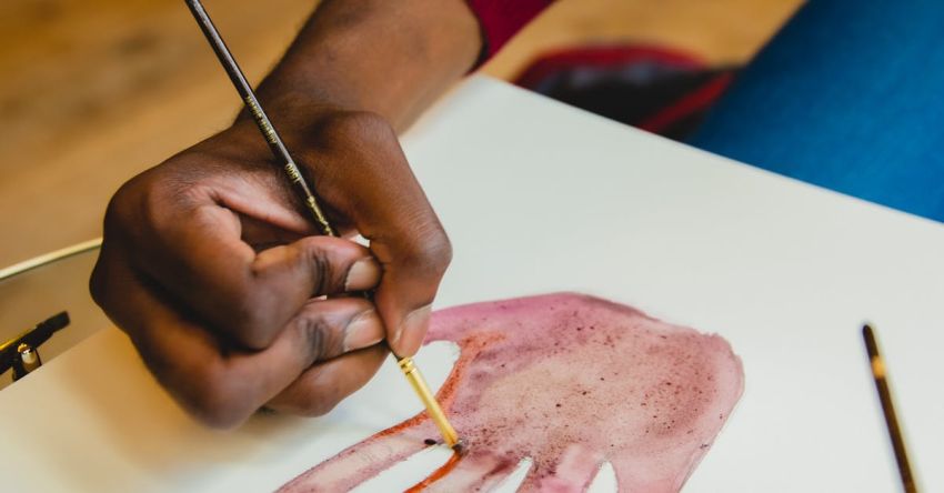 Painting Techniques - From above of anonymous African American male painter with brush drawing palm of head while sitting at table on blurred background