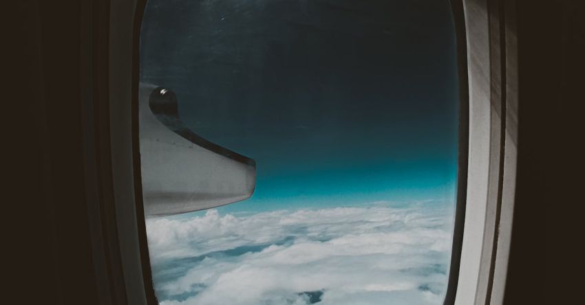 Traveling Abroad - Porthole view of blue sky with fluffy white clouds and airplane turbine during flight